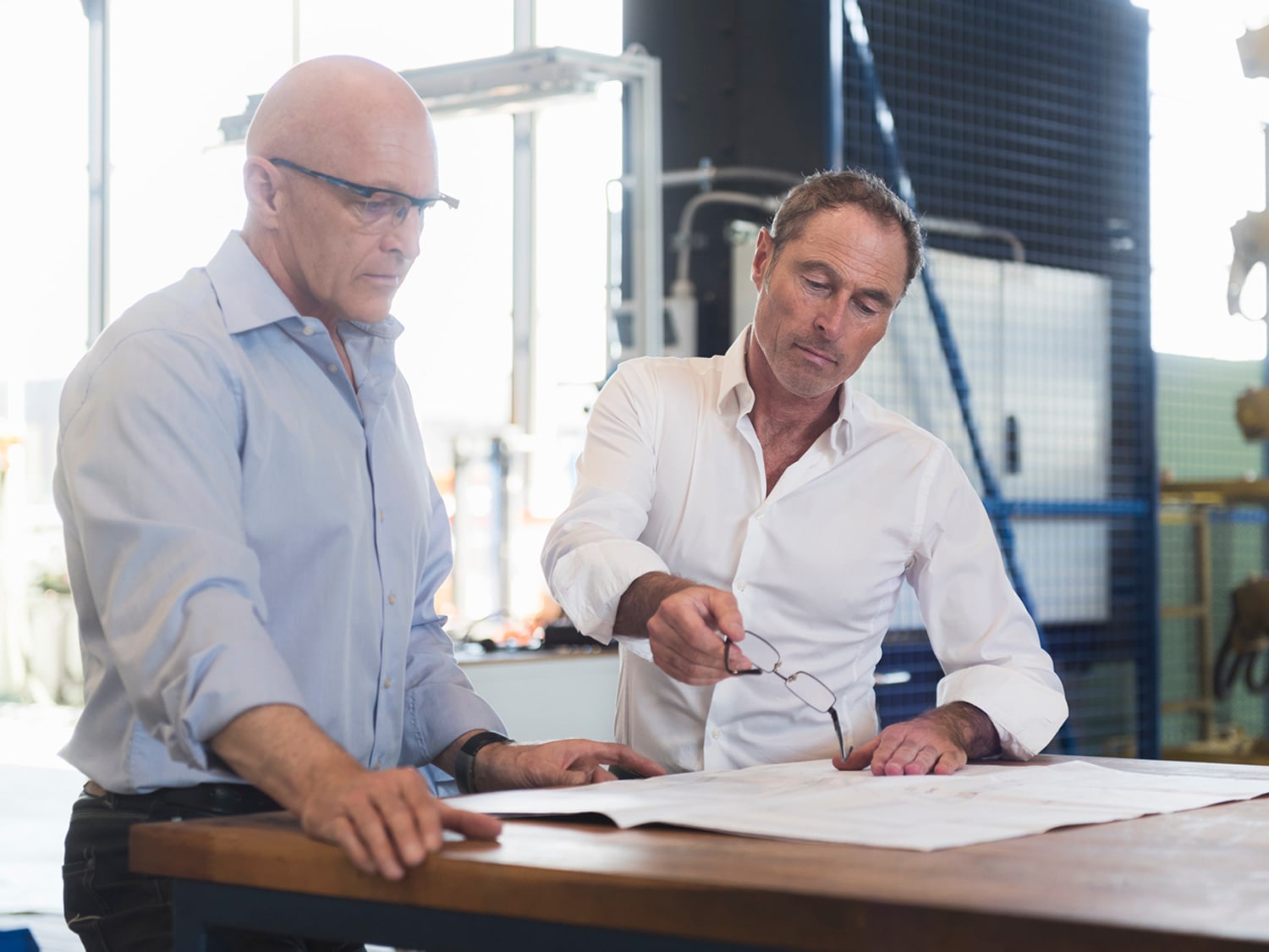 Two men looking at technical designs on a table and pointing to them.